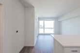 This modern single-floor residence showcases a clean, contemporary design throughout, characterized by crisp white walls, warm wood-tone flooring, and an abundance of natural light. The open-concept layout seamlessly connects the kitchen and living area, creating a spacious and functional flow. The kitchen is well-equipped with stainless steel appliances, including a refrigerator, electric range, microwave, and dishwasher, complemented by sleek white cabinetry, light countertops, and an integrated sink. A peninsula counter serves as a natural divider between the kitchen and the open living space, ideal for casual dining or entertaining. Large floor-to-ceiling windows in the living area and bedroom invite generous natural light and offer views of the surrounding landscape and treeline, enhancing the airy ambiance of the space. The bedroom features plush carpeting and a sizable window that frames the outdoor scenery. The bathroom is finished in a clean, minimalist style with a full tub-shower combination featuring tiled surround, a white vanity with undermount sink, and warm hardwood-style flooring. Recessed lighting throughout maintains a bright and inviting atmosphere across the entire residence.