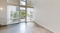 This contemporary two-story residence in Seattle's Queen Anne neighborhood offers a thoughtfully designed layout across two levels. The main floor features polished concrete floors throughout, lending an industrial-modern aesthetic to the open living area. Floor-to-ceiling windows and a glass entry door flood the living space with natural light and provide views of lush greenery outside. A bold red entry door adds a striking accent to the otherwise clean, minimalist interior.

The kitchen is well-equipped with stainless steel appliances including a range, microwave, and refrigerator, complemented by a two-tone cabinetry scheme of white upper cabinets and dark lower cabinets, finished with a classic subway tile backsplash. Track lighting overhead enhances the functional workspace. Two bathrooms serve the home — one on the main floor with polished concrete flooring and a dark-vanity, and a second featuring a full tub-shower combination.

A staircase leads to the upper level, where the bedroom is carpeted and benefits from a window with neighborhood views. The upper floor also features an open loft-style railing, adding architectural interest. Additional conveniences include in-unit laundry and two closets, completing this efficient and stylish urban home.