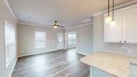 This single-story home on Old Monrovia Road NW in Huntsville, Alabama, presents a clean, modern aesthetic throughout its open-concept layout. Crown molding frames each room, complementing the neutral gray-beige palette that lends a cohesive, contemporary feel across the entire space.

The living area is bright and generously proportioned, benefiting from multiple windows dressed with white blinds that allow ample natural light. A ceiling fan with a wood-toned finish anchors the room, while durable hardwood-style flooring extends seamlessly into adjoining spaces, reinforcing the open flow of the floor plan.

The kitchen is well-equipped and thoughtfully designed, featuring white shaker-style cabinetry, granite countertops, and a full suite of stainless steel appliances including a range, over-the-range microwave, dishwasher, and refrigerator. A kitchen island with pendant lighting above provides additional workspace and serves as a natural transition point to the living area.

The bedrooms are comfortably sized, each with hardwood-style flooring, ceiling fans, natural light from well-positioned windows, and access to closet space. The bathroom includes a walk-in shower enclosed by dark-framed glass doors with a built-in seat, offering a clean, functional design.

Overall, the home presents a bright, move-in-ready environment with consistent finishes and a practical single-floor layout.