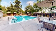 Located at 2309 Rock St in Mountain View, California, this pool and recreation facility offers a well-appointed, single-floor layout designed to support an inviting outdoor experience. The interior consists of connecting hallways that guide visitors seamlessly between the two full bathrooms, each finished with clean tile flooring, a classic pedestal sink, framed mirror, overhead vanity lighting, and a wall-mounted paper towel dispenser. One bathroom also features a glass-enclosed shower stall, adding additional functionality for pool users. The neutral, light-toned walls and tiled surfaces throughout create a bright, sanitary, and welcoming atmosphere. The focal point of the property is the expansive outdoor swimming pool, featuring vivid turquoise water and a clearly marked lap lane. The pool deck is finished in light concrete and is generously furnished with lounge chairs and shaded umbrella stations, providing ample space for relaxation. The entire area is enclosed by a warm cedar-toned wooden fence, offering privacy while mature trees provide natural shade and a lush green backdrop. A small poolside structure serves as a recreation or utility room, adding to the facility's amenities. The combination of well-maintained interior facilities and a resort-like outdoor setting makes this a highly functional and enjoyable recreational space.