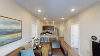 This single-floor unit offers a thoughtfully designed open-concept layout connecting the living and kitchen areas. The kitchen is outfitted with dark espresso cabinetry, granite countertops, stainless steel appliances including a refrigerator, range, and over-the-range microwave, and a peninsula with bar seating — ideal for casual dining. Recessed lighting illuminates the space, which also features wood-look flooring carried consistently throughout.

The living area comfortably accommodates multiple seating arrangements and includes a door providing direct exterior access with natural light. Multiple bedrooms are present, each with a ceiling fan, window with exterior views, and sufficient space for a bed and study area. One bedroom features soft, neutral tones with a large decorative window, while another includes a dedicated desk workspace.

The bathroom features a dark-framed vanity with granite countertop and undermount sink, a framed mirror, and brushed nickel fixtures. The overall ambiance is clean and contemporary, with neutral wall tones, consistent flooring, and a practical layout well-suited for shared or multi-occupant living.