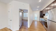 Located at 36 Village Place in Ithaca, NY, this single-floor unit offers a clean, modern aesthetic defined by light hardwood-style flooring, crisp white walls, and recessed lighting throughout. The open living area is generously proportioned, bathed in natural light, and equipped with a wall-mounted mini-split system for efficient climate control. A ceiling fan adds additional comfort to the space.

The kitchen is a functional highlight, featuring rich dark-stained cabinetry extending from floor to ceiling, granite-look countertops, and a full suite of stainless steel appliances including a range, built-in microwave, dishwasher, and refrigerator. A double-basin sink sits beneath recessed lighting, and a glass-panel exterior door floods the kitchen and entryway with natural light.

The bedroom is a comfortable, well-lit space with its own wall-mounted mini-split unit, a ceiling fan, and a window with blinds. The bathroom continues the cohesive design language with a dark wood vanity, a large mirror, contemporary light fixtures, and light flooring. Throughout the unit, the consistent use of neutral tones and quality finishes creates a cohesive and inviting living environment.