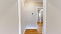 This three-story home offers five bedrooms and three bathrooms distributed across well-defined levels. The ground floor, the most compact level, houses a garage with a paneled door, concrete flooring, and clean white walls, alongside entry hallways finished with light hardwood flooring and crisp white trim and baseboards.

The main living level is the most expansive floor, featuring a combined kitchen and living room. The living area is brightened by a large bank of double-hung windows, hardwood floors, crown molding, recessed lighting, and a ceiling fan. The kitchen is appointed with white cabinetry, granite countertops, a subway tile backsplash, and stainless steel appliances.

The upper floor contains additional bedrooms, including a generously sized primary bedroom with a dedicated closet, and is finished with plush carpet. Hallways throughout the home are clean and neutral, with warm wood flooring and a thermostat-integrated smart panel.

The bathrooms feature marble-look porcelain tile flooring, white vanities with granite countertops, oval mirrors, and glass-enclosed walk-in showers clad in large-format marble-style tiles with mosaic tile flooring. Natural light enters through double-hung windows, contributing to the home's bright, cohesive aesthetic.