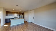 This single-floor unit is designed with a contemporary, open-concept layout that seamlessly connects the kitchen and living areas. The kitchen is a standout feature, equipped with dark espresso cabinetry extending to the ceiling for ample storage, a white subway tile backsplash, and a full suite of stainless steel appliances including an electric range, built-in microwave, and French door refrigerator. A large granite-topped island with an undermount sink serves as both a functional workspace and a casual dining area, illuminated by two decorative pendant lights overhead.

The living area is open and well-proportioned, finished with warm hardwood-style flooring throughout and neutral-toned walls that contribute to a clean, modern aesthetic. A glass-paneled door provides access to an outdoor space while allowing natural light to fill the room.

The bedroom is carpeted for comfort and features dual windows overlooking the exterior, a ceiling fan, and a dedicated closet with a built-in hanging rod. A nearby full bathroom offers a tub-shower combination with brushed nickel fixtures, wood-look flooring, and a small window for natural light. The unit also includes a closeted storage area near the entryway, adding to the overall functionality of the space.