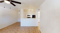 This single-floor residence offers a thoughtfully designed open-concept layout that makes efficient use of its space. The living area is anchored by warm beige tile flooring that extends throughout the main living spaces, complemented by a ceiling fan with a light fixture overhead. A defining architectural feature is the raised pass-through kitchen, framed by a half-wall partition that creates a natural visual separation while maintaining an open feel between the kitchen and living area. The kitchen is equipped with white shaker-style cabinetry, granite-look countertops, a black refrigerator, an electric range with a range hood, and track lighting that illuminates the workspace. A sink with additional counter space lines the adjacent wall, completing the functional kitchen setup. The bedroom features plush wall-to-wall carpeting, a ceiling fan, and a window with horizontal blinds that allows natural light to filter in while providing privacy. A second room with tile flooring and a ceiling fan offers flexible use as an additional bedroom or living space, also benefiting from a natural light-filled window. The bathroom is finished with tile flooring, a white vanity with granite-style countertops, a mirrored medicine cabinet, and a full shower-tub combination. A hallway with a bifold-door closet adds practical storage. Overall, the space presents a clean, functional, and comfortable living environment.