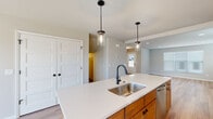 This three-floor home is thoughtfully designed with a clean, modern aesthetic carried consistently throughout. The main living level centers on an open-concept layout where the kitchen and living area flow seamlessly together, finished with light-toned hardwood flooring that enhances the sense of space. The kitchen is well-appointed with warm wood cabinetry, stainless steel appliances including a refrigerator, range, and microwave, and a central island topped with white countertops. A double undermount sink with a matte black faucet anchors the island, which is illuminated by two pendant lights with glass shades. Natural light enters through multiple windows fitted with horizontal blinds. A dedicated entry area provides convenient access to the main level.

Upper-floor bedrooms are carpeted for comfort and include ceiling fans, sliding closet doors with built-in shelving, and neutral wall tones. A full bathroom on this level features a wood-toned vanity, white countertop, large mirror, and a glass-enclosed shower. A dedicated laundry area accommodates a full-size washer and dryer with overhead shelving. The lower level includes a spacious attached garage with a sectional door and concrete flooring, offering substantial storage and parking capacity.