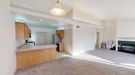 This single-story space is designed with an open, functional layout that connects the main living and kitchen areas seamlessly. The living room is a generous, carpet-floored space highlighted by a green marble-surround fireplace as its focal point, with vaulted ceiling elements and access to a sliding glass door with vertical blinds that allows natural light to flow in.

The kitchen is well-equipped with warm wood cabinetry, a built-in peninsula that provides additional counter space and casual seating potential, light-toned laminate countertops, black appliances including a range and built-in microwave, a stainless steel refrigerator, and a utility sink. Light tile flooring extends throughout the kitchen area.

The bedrooms are carpeted and neutrally finished, each offering closet storage. One bedroom features a double sliding closet with natural light from a window, while another is a versatile, roomy space with its own closet and large window with vertical blinds.

The bathrooms include a full bath with a tub/shower combination, wood vanity cabinetry, and tile flooring. A dedicated in-unit laundry closet with a full-size washer and dryer adds everyday convenience.