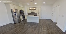 Located on the fourth floor at 1070 River Rd in New Milford, NJ, this 1,090-square-foot apartment offers a well-designed two-bedroom, two-bathroom layout with modern finishes throughout. Dark hardwood-style flooring runs continuously across the entire unit, creating a cohesive and polished aesthetic against the crisp white walls and clean baseboards.

The combined kitchen and living room serves as the heart of the home. The kitchen is a standout feature, boasting tall cream-colored cabinetry with glass-front upper panels, a mosaic tile backsplash, stainless steel appliances including a French door refrigerator and electric range, and a sleek center island with a white countertop topped by a modern pendant light fixture.

The primary bedroom measures 190 square feet and includes a closet and a wall-mounted HVAC unit, with windows offering views of lush greenery. The second bedroom is equally bright, also benefiting from natural light through windows overlooking the outdoors. Both bathrooms are finished with classic white subway tile — one featuring a glass-enclosed walk-in shower and the other a full soaking tub with shower combination. Two hallways connect the spaces efficiently, completing this clean, contemporary apartment.