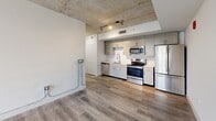 Located on the 8th floor in the heart of Miami's Brickell neighborhood, this 2-bedroom, 2-bathroom unit offers a modern urban living experience with distinctive industrial-inspired design elements. The open layout connects the kitchen and living areas seamlessly, all unified by durable wood-style flooring throughout.

The kitchen is well-appointed with light gray cabinetry, white quartz countertops, a deep undermount sink with a sleek industrial-style faucet, and a full suite of stainless steel appliances including a French door refrigerator, electric range, and built-in microwave. A striking exposed concrete ceiling adds an industrial character to the main living area, complemented by recessed track lighting.

The primary bedroom is generously sized and features floor-to-ceiling windows that frame views of the Miami skyline and surrounding palm-lined streets, allowing for abundant natural light. The second bedroom also benefits from the exposed concrete ceiling aesthetic and direct access to the main living space.

Both bathrooms are finished with wood-look tile flooring, neutral stone-tiled tub-shower combinations, white vanities with undermount sinks, and clean white walls. A dedicated closet provides additional storage. The overall ambiance is clean, contemporary, and well-suited to the vibrant Miami urban lifestyle.