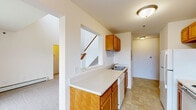 This two-story residence at Coopers Landing Drive in Kalamazoo, Michigan offers a well-organized layout spread across two levels. The main floor comprises the primary living areas, including a combined kitchen and living room, with the upper level dedicated to the bedroom and bathroom.

The kitchen is designed in a galley style, featuring warm honey-toned wood cabinetry both above and below the counters, white appliances including an electric range and refrigerator, a double-basin sink, and light tile flooring. A pass-through counter connects the kitchen to the adjacent living area, adding an open, functional feel.

The living room is notably spacious, boasting soaring ceilings that create a striking sense of volume. A sliding glass door floods the space with natural light and provides outdoor views, while a wall-mounted air conditioning unit and baseboard heating ensure year-round comfort. Neutral carpet covers the floor throughout the living and bedroom areas.

The upper level houses the bedroom, a comfortably sized room with a window offering outdoor views, soft carpeting, and a closet with bi-fold wood panel doors. The full bathroom includes a tub-shower combination, a wood-vanity with a single sink, a large mirror, and tile flooring. A carpeted staircase connects both levels, with hallways providing efficient circulation throughout.