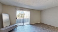 This single-floor unit offers a practical and well-maintained layout designed for comfortable everyday living. The main living area is bright and open, finished with light gray wood-look laminate flooring that extends throughout the space. A full-width sliding glass door fitted with vertical blinds fills the room with natural light and provides direct access to an outdoor area, offering views of greenery beyond. A textured popcorn ceiling and neutral beige walls create a clean, understated backdrop throughout the living space, which also features an accent wall with a subtle brick texture.

The kitchen is efficiently laid out with white cabinetry, dark granite-style countertops, a built-in range, and a full-size refrigerator. A pendant light fixture hangs above the adjacent dining or prep area, adding a decorative touch to the functional space. The transition between the kitchen and living area is seamless, supported by the continuous flooring.

The bathroom features white under-sink cabinetry paired with a dark speckled granite-style countertop and an integrated oval basin. A medicine cabinet with mirrored doors adds storage utility. Overall, the unit presents a clean, move-in-ready environment with cohesive finishes and a straightforward single-level floor plan.