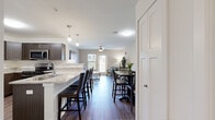 Located on W Casey Dr in Rogers, Arkansas, this single-floor residence offers a thoughtfully designed open-concept layout that seamlessly connects the kitchen, dining, and living areas. The kitchen is outfitted with dark espresso cabinetry, light granite countertops, stainless steel appliances including a refrigerator, range, and microwave, and a breakfast bar with pendant lighting that invites casual seating. Rich wood-style flooring flows throughout the main living areas, adding warmth and continuity to the space. The dining area comfortably accommodates a full dining set and is accented by a round wall mirror, while the living room features generous natural light from a large window and exterior door, a ceiling fan, and a welcoming layout anchored by neutral tones. The bedroom is carpeted for comfort and is equipped with a ceiling fan, providing a calm and restful retreat. The bathroom features wood-style flooring, dark vanity cabinetry with a granite countertop, and clean white walls that keep the space bright and functional. Throughout the unit, a consistent palette of warm neutrals, modern fixtures, and quality finishes creates a cohesive and contemporary ambiance well-suited for everyday living.
