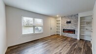 This two-story, 2-bedroom, 2-bathroom home offers a thoughtfully designed layout spread across two floors of comparable size. The main level features a bright living room with rich hardwood-style flooring, a large window that invites natural light, built-in shelving, and a striking stacked-stone accent wall housing a sleek electric fireplace — a clear focal point of the space. The kitchen is well-equipped with dark espresso cabinetry, marble-look quartz countertops, stainless steel appliances including a refrigerator, microwave, and dishwasher, pendant lighting, and a peninsula with a sink — ideal for both cooking and casual dining. A dedicated utility room and hallway complete the lower level. Upstairs, the primary bedroom is generously proportioned, featuring plush carpeting, a ceiling fan, and multiple windows that bathe the room in natural light. The second bedroom includes built-in closet doors and soft carpeting. Both bathrooms are finished with dark vanity cabinetry, quartz countertops, and wood-look tile flooring; one features a full tub-shower combination with large-format marble-style tile surround. The home's neutral color palette and consistent modern finishes create a cohesive, move-in-ready aesthetic throughout.