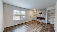 This two-story, 2-bedroom, 2-bathroom home offers a thoughtfully designed layout spread across two floors of comparable size. The main level features a bright living room with rich hardwood-style flooring, a large window that invites natural light, built-in shelving, and a striking stacked-stone accent wall housing a sleek electric fireplace — a clear focal point of the space. The kitchen is well-equipped with dark espresso cabinetry, marble-look quartz countertops, stainless steel appliances including a refrigerator, microwave, and dishwasher, pendant lighting, and a peninsula with a sink — ideal for both cooking and casual dining. A dedicated utility room and hallway complete the lower level. Upstairs, the primary bedroom is generously proportioned, featuring plush carpeting, a ceiling fan, and multiple windows that bathe the room in natural light. The second bedroom includes built-in closet doors and soft carpeting. Both bathrooms are finished with dark vanity cabinetry, quartz countertops, and wood-look tile flooring; one features a full tub-shower combination with large-format marble-style tile surround. The home's neutral color palette and consistent modern finishes create a cohesive, move-in-ready aesthetic throughout.