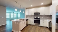 Located at 1161 3rd Ave E in Bradenton, Florida, this single-story home offers a thoughtfully designed open-concept layout that seamlessly connects the main living areas. The kitchen is a standout feature, showcasing crisp white shaker cabinetry, granite-look countertops, a neutral tile backsplash, and a full suite of stainless steel appliances including a refrigerator, range, microwave, and dishwasher. A peninsula with an undermount sink and pendant lighting overhead creates a natural transition into the living and dining areas, which are accented by a bold teal accent wall and recessed lighting. Rich wood-look vinyl plank flooring extends throughout the main living spaces, providing both durability and warmth. The spacious living room features multiple windows with blinds that invite abundant natural light, complemented by a ceiling fan overhead. Bedrooms are carpeted for comfort and include windows that overlook the surrounding landscape. The primary bathroom offers a glass-enclosed walk-in shower, white vanity cabinetry, and wood-look flooring, while a secondary bathroom includes a tub-shower combination with tile surround and a matching vanity. The overall aesthetic is clean, contemporary, and move-in ready.