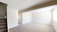 This two-floor residence offers a practical and well-organized layout designed for comfortable everyday living. The main living area is generously sized, featuring plush wall-to-wall carpeting, neutral-toned walls, and a textured ceiling that adds subtle character. Structural beams define the open layout, and natural light filters in through slatted window blinds, creating a bright and welcoming atmosphere throughout.

The kitchen is efficiently designed with crisp white cabinetry, light granite-style countertops, and light wood-style vinyl flooring. Black appliances — including an electric range, refrigerator, and dishwasher — provide a clean contrast to the white cabinetry, while a stainless steel sink completes the functional workspace.

The bedrooms are carpeted and well-proportioned, each featuring windows that allow ample natural light and outdoor views. The neutral color palette and textured ceilings carry throughout, maintaining a cohesive aesthetic across the space.

The bathroom includes a full-size soaking tub with an overhead shower, clean white surround, and chrome fixtures. A dedicated utility room houses a water heater, wire shelving, and hookups, offering practical storage and laundry provisions. Overall, this space presents a clean, move-in-ready environment with consistent finishes across both floors.