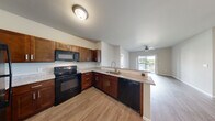 Located at 1913 E 44th St in Joplin, Missouri, this well-designed 3-bedroom, 2-bathroom single-story home offers a comfortable and functional layout. The open-concept kitchen is a standout feature, boasting rich warm-toned cabinetry, granite-style countertops, a peninsula with a sink, and black appliances including a range, built-in microwave, dishwasher, and refrigerator. Light wood-style flooring flows through the kitchen and into the combined dining and living area, which is brightened by natural light and features a ceiling fan. Sliding glass doors lead to a private balcony overlooking an open, scenic outdoor landscape. The three bedrooms are carpeted for comfort, each equipped with ceiling fans and ample natural light from well-placed windows. The primary bedroom offers direct access to a bathroom with granite-topped vanity and a dedicated walk-in closet fitted with wire shelving. Five total closets throughout the home provide generous storage. The bathrooms echo the warm cabinetry and granite finishes seen in the kitchen. A utility room and a hallway round out the floor plan, while neutral wall tones and consistent finishes throughout contribute to a cohesive, move-in-ready aesthetic.