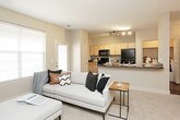 This single-floor residence offers a practical and comfortable layout designed to maximize everyday living. The kitchen is outfitted with light maple cabinetry, dark granite-style countertops, and a full suite of black appliances — including a refrigerator, electric range, microwave, and dishwasher — all set atop rich hardwood flooring that adds warmth to the space. Adjacent to the kitchen, a compact dining nook features a round wood table beneath a modern multi-pendant chandelier, creating an intimate setting for meals. The living area is carpeted and inviting, centered around a wall-mounted flat-screen TV above a dark media console, with natural light filtering in through a large window fitted with horizontal blinds. An elegant arched doorway connects the living space to the rest of the unit. Both bedrooms are carpeted and equipped with ceiling fans, offering a restful atmosphere. One bedroom includes a built-in desk and direct access to a private bathroom, while the other benefits from a large window that brings in generous natural light. The full bathroom features tile flooring, a combined tub and shower enclosure with glass doors, a vanity with ample storage, and neutral tile accents — delivering a clean, functional finish throughout.