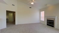 This single-floor space is thoughtfully designed to maximize comfort and functionality. The main living area immediately draws the eye upward with its vaulted ceilings, which lend a sense of spaciousness and airiness to the interior. A ceiling fan with an integrated light fixture is centrally positioned, ensuring both air circulation and ambient lighting throughout the room.

The flooring throughout the living area consists of plush, neutral-toned wall-to-wall carpeting, providing a soft and comfortable underfoot experience. The walls are finished in a clean, light neutral tone that enhances the brightness of the space and creates a versatile backdrop suitable for a variety of interior styles.

Natural light enters the room through a window fitted with blinds, offering both illumination and privacy control. The window's placement allows for a pleasant view outward while keeping the interior well-lit during daylight hours. Ventilation is further supported by ceiling-mounted HVAC vents, reflecting a practical and well-considered layout.

A doorway leads to an additional area of the space, suggesting a connected floor plan that facilitates easy movement between rooms. The overall ambiance of the space is clean, open, and inviting, making it a comfortable and adaptable environment ready to accommodate a range of furnishing and lifestyle preferences.
