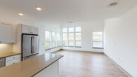 Located along Manhattan Boulevard in Dayton, Kentucky, this single-floor residence offers a clean, modern design with an open-concept layout and consistent light wood flooring throughout. The expansive living area is defined by a striking bank of floor-to-ceiling windows that frame panoramic views of the Ohio River and surrounding landscape, filling the space with abundant natural light. An additional side window further enhances the bright, airy atmosphere.

The well-appointed kitchen is a standout feature, outfitted with crisp white shaker-style cabinetry, white subway tile backsplash, quartz countertops, a center island, and a full suite of stainless steel appliances including a French door refrigerator, dishwasher, microwave, and electric range. The layout provides generous counter and storage space ideal for everyday cooking.

The bedrooms are bright and comfortable, with one featuring a ceiling fan and dual windows offering scenic outdoor views, and another with high transom windows that allow natural light while maintaining privacy. Closet space is provided with built-in shelving. The bathroom includes a tub and shower combination, an undermount sink with quartz vanity, and hardwood-style flooring that ties seamlessly into the rest of the residence.