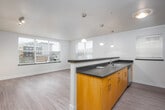 This single-floor residence offers a clean, modern layout designed for comfortable everyday living. The heart of the home is an open-concept kitchen and living area, where light wood-tone flooring flows seamlessly throughout. The kitchen features a generous curved peninsula with a dark countertop, ideal for casual dining or entertaining. Stainless steel appliances — including a refrigerator, electric range, and over-the-range microwave — are complemented by warm wood cabinetry and ample upper storage. Pendant lighting above the peninsula adds a warm, inviting glow to the space. A bright window allows natural light to fill the kitchen area.

The living space extends openly from the kitchen, creating a spacious and airy feel. A carpeted bedroom offers a quiet retreat, with a large window fitted with blinds that brings in natural light while providing privacy. Baseboard heating ensures year-round comfort in this room.

The unit includes two bathrooms, both finished with light wood-look flooring and white cabinetry. One bathroom features a walk-in shower with a glass sliding door and chrome fixtures, while the other includes a toilet and vanity with a wide mirror. A well-lit hallway with track lighting connects the rooms, completing this thoughtfully designed and move-in ready space.