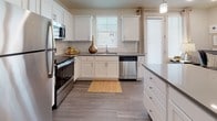 This single-floor residence offers a thoughtfully designed layout that balances functionality and comfort. The kitchen is a standout feature, equipped with stainless steel appliances including a refrigerator, range, microwave, and dishwasher. White shaker-style cabinetry pairs with grey countertops and a classic subway tile backsplash, while wood-look flooring and natural light from multiple windows contribute to a bright, welcoming atmosphere. A kitchen island provides additional prep and storage space.

The living area features the same wood-look flooring and offers a comfortable, open setting suitable for both relaxing and entertaining. The bedrooms are carpeted for warmth and comfort, each benefiting from natural light through large windows fitted with blinds and drapery. Ceiling fans add to the functionality of the sleeping spaces.

The bathroom is finished with white shaker vanity cabinetry, grey countertops, a large mirror, and wood-look flooring, complemented by a shower-tub combination. The space also includes a dedicated laundry area housing a full-size top-load washer and dryer with overhead shelving for added storage convenience. Overall, the residence presents a clean, modern aesthetic with consistent finishes throughout.