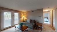 Located at 5051 Open Meadows Dr in Columbus, Ohio, this single-floor residence offers a well-organized layout with comfortable living spaces throughout. The living room serves as the heart of the home, featuring plush carpeting, warm neutral-toned walls, and a set of French-style patio doors that invite natural light and provide direct outdoor access. The galley-style kitchen is efficiently designed with rich dark cabinetry lining both sides, light countertops, wood-look flooring, and white appliances including an electric range, dishwasher, and refrigerator — offering ample storage and workspace. The bedroom is generously proportioned, with soft carpeting, warm beige walls, a textured ceiling, and a window that brings in natural light. A closet provides convenient built-in storage. The full bathroom is neatly appointed with a single-sink vanity featuring a white countertop, a framed mirror, a toilet, and a tub-shower combination with a curtain, all set against textured neutral walls and complemented by wood-look flooring. The overall ambiance of this home is warm and functional, with consistent neutral tones and practical finishes creating a cohesive and inviting atmosphere throughout.