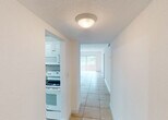 Located in Miami, FL, this single-floor residence offers a clean, bright, and efficiently laid-out living environment. Light-colored ceramic tile flooring runs consistently throughout the entire space, lending a cohesive and easy-to-maintain aesthetic.

Upon entry, a welcoming foyer with a solid front door leads into the main living areas. The spacious living room is bathed in natural light from a large window fitted with vertical blinds, offering views of lush greenery outside. A ceiling fan adds comfort to the room's airy atmosphere.

The kitchen is well-equipped, featuring white raised-panel cabinetry that extends to the ceiling for generous storage, granite countertops, a stainless steel sink, and white appliances including a refrigerator, dishwasher, stove, oven, and an over-the-range microwave. Track lighting illuminates the workspace effectively.

A hallway connects the living areas to the bedrooms. Each bedroom is comfortably sized with white walls, tile flooring, and closets with louvered bifold doors. The bathroom is neatly appointed with recessed lighting, a tiled shower-tub combination with glass sliding doors, and granite countertop details that echo the kitchen's finishes.

Overall, the space presents a bright, functional, and well-maintained interior well-suited for comfortable South Florida living.