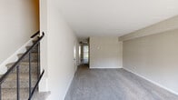 Located at 470 Youngs Mill Ln in Newport News, Virginia, this two-story home offers a clean, neutral aesthetic throughout. The main level features a generously sized living area finished with plush grey carpeting and crisp white walls, allowing ample natural light to filter through. A staircase with dark metal balusters connects the two floors, adding a subtle design element to the interior. The galley-style kitchen is well-appointed with white shaker cabinetry, quartz countertops featuring subtle speckled detailing, and wood-look flooring. Black appliances, including a refrigerator, dishwasher, and range, complement the bright cabinetry, while overhead storage maximizes functionality. The upper level hosts carpeted bedrooms dressed in warm neutral tones. Several rooms feature windows with blinds that invite natural light and outdoor views of the surrounding neighborhood. Bedrooms include closet space, with at least one room offering a dedicated walk-in-style closet with shelving. Throughout the home, clean lines, neutral paint tones, and consistent flooring choices create a cohesive and move-in-ready atmosphere.