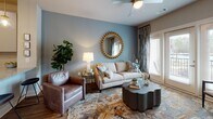 Located at Eagle Hall Lane in Goose Creek, South Carolina, this single-story residence offers a thoughtfully designed layout visible across its interconnected living spaces. The living room serves as the centerpiece of the unit, featuring warm hardwood-style flooring, a ceiling fan, and French doors that open to a balcony, allowing natural light to fill the space. Neutral walls are accented by a soft blue feature wall, creating a calm, inviting atmosphere complemented by patterned drapery and a decorative area rug.

The kitchen is outfitted with modern gray flat-front cabinetry, granite-style countertops, a subway tile backsplash, and a full suite of stainless steel appliances, including a side-by-side refrigerator, range, and over-the-range microwave. The layout provides functional counter space and ample storage.

Two bedrooms each feature plush carpeting, large windows with blinds and coordinating curtains that bring in natural light and outdoor views, and sufficient space for full bedroom furnishings. The bathroom includes hardwood-style flooring, a granite-topped vanity with gray cabinetry, and a full tub-shower combination with a curved curtain rod. The overall aesthetic throughout is cohesive, modern, and residential.