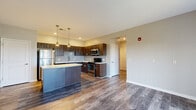 Located at 1009 Meadow Ln in Canonsburg, PA, this 2-bedroom, 1-bathroom residence offers a thoughtfully designed single-floor layout with modern finishes throughout. The open-concept kitchen and living area serves as the heart of the home, showcasing bold wood-grain cabinetry, a subway tile backsplash, white quartz countertops, and a full suite of stainless steel appliances. A central kitchen island with pendant lighting above provides additional prep space and a natural gathering point. Rich hardwood-style flooring flows seamlessly through the kitchen, living, and hallway areas, adding warmth and cohesion to the space. The living room benefits from a sliding glass door that floods the room with natural light and provides access to an outdoor area with exterior views. The primary bedroom is a comfortable, generously sized retreat featuring plush carpeting and a walk-in closet equipped with wire shelving for organized storage. The second bedroom also features soft carpeting and neutral tones. The shared bathroom is finished with a dark wood-grain vanity, white countertop, a large mirror with modern lighting, and hardwood-style flooring, tying in the design language of the rest of the home. A connecting hallway links all rooms efficiently, completing this clean and contemporary single-level layout.