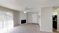 This single-floor residence offers a well-organized and functional layout throughout. The living area serves as the heart of the home, featuring a classic white brick fireplace that anchors the space with warmth and character. A ceiling fan with integrated lighting provides both comfort and illumination, while neutral-toned carpet and soft wall colors create a clean, welcoming atmosphere. A textured popcorn ceiling adds a traditional finish overhead. The entry door opens directly into this main living space, which connects seamlessly to the kitchen area via an open pass-through layout. The kitchen is equipped with dark appliances, including a refrigerator, and is framed by white cabinetry, with a convenient built-in shelf visible near the partition wall. The bathroom features a granite-style countertop with an undermount sink, a framed mirror, and textured walls that add subtle visual depth. Multiple carpeted bedrooms offer comfortable, quiet retreats, each with neutral walls, adequate natural light through slatted blinds, and closet access. The consistent use of soft, neutral tones throughout the space creates a cohesive and move-in-ready environment suited for everyday living.