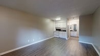 This single-floor studio-style unit offers a practical and efficiently designed layout that maximizes every square foot of available space. The open main area seamlessly combines the living room and kitchen, creating a unified, easy-to-navigate floor plan. Durable vinyl plank flooring in a warm gray-brown tone runs throughout the unit, providing a cohesive look that is both stylish and easy to maintain. Neutral taupe-toned walls complement the clean white baseboards, giving the space a fresh and modern feel.

The kitchen is neatly integrated into the main living area and features white cabinetry, dark countertops, a white range with overhead microwave, and a refrigerator, offering all the essentials in a compact footprint. A textured ceiling adds a layer of visual detail throughout the unit.

The unit includes two bathrooms. One bathroom features a white vanity with a dark countertop, a large mirror with overhead lighting, and access to an adjacent space with a full bathtub and tiled surround. A hallway connects these areas, flanked by a closet, providing useful storage.

Natural light enters through a window in the main living area, accompanied by a wall-mounted HVAC unit. The entry door opens directly into this bright, open living space, rounding out a functional and well-appointed unit.