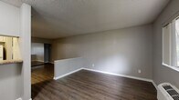 This single-floor unit offers an efficient and well-organized layout, comprising a living room, a kitchen area, and a full bathroom. The living room is an open, versatile space finished with rich, dark hardwood-style flooring and neutral gray walls, creating a clean and modern aesthetic. A textured popcorn ceiling adds a classic touch throughout the main living area. A low half-wall partition subtly separates zones within the space, while a built-in closet provides practical storage. Large windows allow generous natural light to fill the room, offering views of surrounding greenery and the exterior of the building. A wall-mounted PTAC heating and cooling unit ensures year-round climate control. The kitchen area, visible in the floorplan, features a compact arrangement with a stove and counter space. The full bathroom is thoughtfully designed with white cabinetry, a granite-style countertop with an undermount sink, a large vanity mirror, and a bathtub-shower combination with tiled surround. Hardwood-style flooring extends into the bathroom, maintaining a consistent design language throughout the unit. Overall, the space presents a functional and tidy interior suited for efficient everyday living.