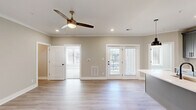 Located in Daleville, Virginia, this thoughtfully designed 2-bedroom, 2-bathroom single-floor home offers a clean, modern aesthetic throughout. The open-concept living, dining, and kitchen area creates a bright, airy atmosphere, anchored by light hardwood-style flooring and neutral warm-toned walls. A stylish ceiling fan with a brushed brass finish and recessed lighting illuminate the living space, which opens to a private balcony through French doors fitted with plantation shutters.

The kitchen is a standout feature, showcasing gray shaker-style cabinetry, crisp white quartz countertops, a large center island with an undermount sink, and stainless steel appliances including a refrigerator, electric range, and built-in microwave. Industrial-style pendant lights add a contemporary touch overhead. A pantry provides additional storage convenience.

The primary bedroom features light wood-style flooring, crown molding, a ceiling fan, and direct access to a private en-suite bathroom with gray cabinetry. The second bedroom is carpeted and includes a double closet with natural light from a large window. Additional highlights include four closets, a dedicated laundry room, and a hallway connecting the well-organized layout seamlessly throughout.