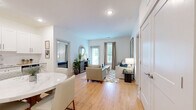 This well-appointed 3-bedroom, 2-bathroom residence in Indian Land, SC offers a thoughtfully designed single-level layout that maximizes functionality and comfort. The open-concept kitchen and living area serves as the heart of the home, featuring crisp white shaker cabinetry, granite countertops, a full suite of stainless steel appliances, and light hardwood flooring that extends throughout the main living spaces. A dedicated dining area with a round marble-top table sits adjacent to the kitchen, making it ideal for everyday meals and entertaining. The living room is bright and welcoming, with large windows dressed in neutral drape panels that invite natural light, and a glass door providing access to the outdoors. Each bedroom is finished with plush carpeting and ceiling fans, with the primary bedroom benefiting from a dedicated walk-in closet. Both bathrooms are outfitted with white shaker vanities, granite countertops, and hardwood-style flooring. A secondary bedroom includes a double-door closet, adding practical storage. The clean, neutral color palette and consistent finishes throughout create a cohesive and modern ambiance, making this residence a comfortable and move-in-ready home in the Jessamine Grove community.