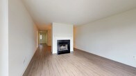 This single-floor residence offers a well-organized layout with a clean, neutral aesthetic throughout. The living room serves as a central gathering space, highlighted by a classic fireplace with a black surround and white mantel, set against crisp white walls and light hardwood-style flooring that extends through the main living areas. A hallway leads toward the entry door, providing a clear sense of the home's linear flow.

A separate room bathed in natural light features large windows and a sliding glass door, allowing outdoor views and generous sunlight to fill the space, further complemented by the same light-toned flooring.

The kitchen is functionally equipped with warm wood cabinetry, stainless steel appliances including a refrigerator and range, and light countertops, all set on matching hardwood-style floors. Storage is well addressed with upper and lower cabinetry throughout.

The bedrooms are finished with plush neutral carpet and feature windows that bring in natural light. One bedroom includes a double window overlooking greenery outdoors.

Two bathrooms serve the residence. One features a wood-toned vanity with granite-style countertop, tub/shower combo, and tile flooring. The second offers a clean, all-white tub/shower unit with chrome fixtures, maintaining a simple and functional design.