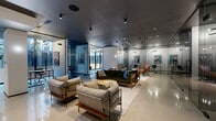 This expansive 3,840 square foot office space in Miami showcases a sleek, modern design that seamlessly blends functionality with style. The open-plan layout is characterized by high ceilings and polished concrete floors, creating a sense of spaciousness and industrial chic. Glass partitions divide the area into distinct zones while maintaining visual connectivity and allowing natural light to permeate throughout.

The space features multiple seating arrangements, including comfortable lounge areas with colorful sofas and armchairs, as well as more formal meeting spaces with elegant wooden tables and chairs. A striking ceiling design with alternating white beams adds visual interest and helps define different areas within the open floor plan.

Artwork adorns the white brick walls, adding personality and color to the space. Strategically placed potted plants bring a touch of nature indoors. The lighting scheme combines recessed ceiling lights, pendant globes, and stylish fixtures to create a well-illuminated and inviting atmosphere.

A standout feature is the custom-built shelving unit that spans one wall, offering ample storage and display space. The overall design ethos balances professionalism with comfort, making it an ideal environment for creative collaboration and productive work.