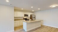 This single-story residence in Columbia, SC offers a thoughtfully designed layout with three bedrooms, two bathrooms, and a seamless open-concept living and kitchen area. The kitchen serves as the heart of the home, showcasing granite countertops, crisp white shaker-style cabinetry, stainless steel appliances, and a central island with a built-in sink — ideal for both cooking and entertaining. Light hardwood-style flooring runs throughout the main living areas, complemented by recessed lighting that keeps the space bright and inviting. A well-connected hallway links the living spaces to the private bedrooms and utility room. The bedrooms feature plush carpeting and ceiling fans, with the primary bedroom offering a generously sized walk-in closet and access to natural light. Sliding glass doors in the living area open to an outdoor balcony, extending the living space and providing views of the surrounding greenery. Both bathrooms are finished with granite vanity countertops, white cabinetry, and full tub-shower combinations. Clean white walls and consistent trim throughout create a cohesive, modern aesthetic. A dedicated utility room and additional closet space add practical storage throughout this well-designed home.