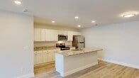 This single-story residence in Columbia, SC offers a thoughtfully designed layout with three bedrooms, two bathrooms, and a seamless open-concept living and kitchen area. The kitchen serves as the heart of the home, showcasing granite countertops, crisp white shaker-style cabinetry, stainless steel appliances, and a central island with a built-in sink — ideal for both cooking and entertaining. Light hardwood-style flooring runs throughout the main living areas, complemented by recessed lighting that keeps the space bright and inviting. A well-connected hallway links the living spaces to the private bedrooms and utility room. The bedrooms feature plush carpeting and ceiling fans, with the primary bedroom offering a generously sized walk-in closet and access to natural light. Sliding glass doors in the living area open to an outdoor balcony, extending the living space and providing views of the surrounding greenery. Both bathrooms are finished with granite vanity countertops, white cabinetry, and full tub-shower combinations. Clean white walls and consistent trim throughout create a cohesive, modern aesthetic. A dedicated utility room and additional closet space add practical storage throughout this well-designed home.