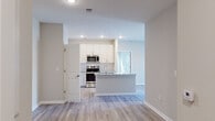Located at 1090 Summersweet Dr in New Bern, NC, this single-story residence showcases a clean, contemporary design with a consistent palette of neutral tones and light wood-look flooring carried throughout every room. The open-concept kitchen serves as a central highlight, outfitted with crisp white cabinetry extending to the ceiling, granite countertops, a subway tile backsplash, and a full suite of stainless steel appliances including a refrigerator, range, and microwave. A kitchen island provides additional prep and seating space, while a dedicated pantry with wire shelving adds practical storage. The living area flows seamlessly from the kitchen, creating a connected and functional layout. Bedrooms are well-proportioned, each featuring ceiling fans with light fixtures and two-panel interior doors. Natural light enters through windows fitted with blinds. The primary bedroom connects to a walk-in closet equipped with multi-level wire shelving and hanging rods. The bathroom features a soaking tub with a tiled surround and brushed nickel fixtures, complemented by granite-topped vanity cabinetry. Clean lines, recessed lighting, and consistent finishes contribute to a cohesive and move-in-ready atmosphere throughout.