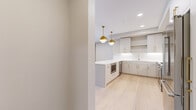 Located in Edina, MN, this well-appointed 2-bedroom, 2-bathroom residence offers a thoughtfully designed single-floor layout with modern finishes at every turn. The heart of the home is a striking open-concept kitchen featuring light gray cabinetry with gold hardware, crisp white quartz countertops, a subway tile backsplash, stainless steel appliances including a gas range and full-size refrigerator, and a large island with a powder-blue base. A pair of globe pendant lights in brushed gold add a refined, contemporary touch overhead, while light-toned hardwood flooring flows seamlessly throughout the main living areas. The spacious primary bedroom offers generous proportions with plush carpeting and large black-framed windows that frame lush outdoor views. The second bedroom similarly features carpet and an oversized window, filling the room with natural light. Both bathrooms are elegantly finished; the primary bath includes a glass-enclosed walk-in shower with tile surround, a floating double vanity with gold hardware, and a backlit mirror. A dedicated laundry area houses a full-size Whirlpool washer and dryer. Clean lines, neutral tones, and upscale hardware choices create a cohesive, modern ambiance throughout this refined Edina residence.
