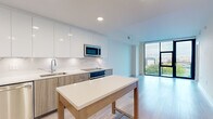 Located in Washington, DC's vibrant Shaw neighborhood, this modern 2-bedroom, 1-bathroom residence offers a thoughtfully designed open-concept layout with contemporary finishes throughout. Light wood-tone flooring flows seamlessly across the entire living space, complementing the bright, neutral palette.

The kitchen and living area form the heart of the home, featuring a sleek, modern kitchen outfitted with high-gloss white upper cabinetry, warm wood-toned lower cabinets, and a marble-style backsplash. Stainless steel appliances — including a refrigerator, dishwasher, wall oven, microwave, and cooktop — complete the space, alongside a central island that provides additional prep and dining space. Floor-to-ceiling windows flood the living area with natural light and frame treetop views of the surrounding neighborhood.

Both bedrooms are well-proportioned and bright, with the primary bedroom benefiting from expansive floor-to-ceiling glass and direct access to an outdoor balcony. The second bedroom offers a clean, versatile space with generous wall area. A dedicated closet provides practical storage.

The bathroom is finished with large-format light tile flooring, subway tile surround in the tub/shower, and warm wood-toned cabinetry. Clean lines and recessed lighting contribute to the overall modern, polished aesthetic throughout this well-appointed residence.