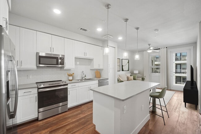 Finish Package II kitchen with stainless steel appliances, white cabinetry, white tile backsplash, grey quartz countertops, and hard surface flooring - Avalon Lowry