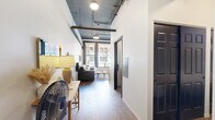 Located in the heart of downtown Spokane at 107 S Howard, this one-bedroom unit offers a thoughtfully designed layout that maximizes every square foot. The open-concept living and kitchen area serves as the core of the space, where light wood-toned cabinetry, a subway tile backsplash, and stainless steel appliances give the kitchen a clean, functional character. A dining area with a wall-mounted TV sits adjacent to the kitchen, making efficient use of the shared space.

The living room benefits from oversized, black-framed windows that frame sweeping views of Spokane's vibrant downtown streetscape, filling the room with natural light. Exposed ductwork and industrial-style pendant lighting on a dark-painted ceiling add an urban, loft-inspired aesthetic that contrasts with the crisp white walls and light hardwood flooring throughout.

A hallway connects the main living area to the private bedroom, which features bold black doors — one leading to the room and two concealing generous closet storage — alongside simple white walls that create a calm, restful atmosphere. The overall ambiance is modern and urban, blending industrial architectural details with clean, contemporary finishes to create a practical and stylish downtown residence.