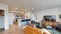 This thoughtfully designed 2-bedroom, 2-bathroom residence spans a single floor and offers a cohesive blend of modern aesthetics and functional living. Light-toned luxury vinyl plank flooring flows throughout the main living areas, anchoring the open-concept layout that connects the living room, dining area, and kitchen seamlessly.

The living room is generously proportioned, featuring large windows dressed with sheer curtains that allow ample natural light to fill the space. The kitchen is outfitted with stainless steel appliances, including a French door refrigerator, electric range, and over-the-range microwave. Light wood cabinetry with matte black hardware pairs with white quartz countertops and a subway tile backsplash, while a kitchen island with bar seating provides additional prep and dining space.

The primary bedroom offers a comfortable retreat with carpeted flooring, a large window with outdoor views, and access to a walk-in closet featuring built-in shelving and hanging rods. The second bedroom is equally well-sized with its own closet. Both bathrooms feature light wood vanities with white countertops and clean, neutral finishes. A dedicated utility room and hallway complete the layout, contributing to the unit's practical organization and efficient use of space throughout.