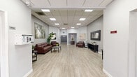 Located at 3560 Flora Vista Ave in Santa Clara, CA, this single-floor commercial suite offers a thoughtfully designed open-plan layout that balances professional functionality with a warm, welcoming ambiance. Light wood-style luxury vinyl flooring runs throughout the space, complementing the soft gray walls and creating a clean, modern aesthetic.

The main area serves as a generously sized lounge and reception zone, furnished with rich burgundy leather seating, dark wood accent tables, and a large rectangular coffee table. A full-length framed mirror anchors one wall, while an open storage console beneath it adds both practicality and style. Lush potted greenery and fresh floral arrangements are thoughtfully placed throughout, adding life and color to the neutral palette.

Large-scale canvas artwork adorns the walls, including nature-inspired prints and cityscapes, contributing to a curated, gallery-like feel. A drop ceiling with recessed skylight panels diffuses bright, even lighting across the entire floor.

Toward the rear of the suite, a corridor leads to additional private areas, including what appears to be a treatment or service room, as well as a niche alcove housing a dark wood cabinet with a stone countertop — ideal for reception or check-in use. The glass entry doors at the front of the suite allow natural light to filter in, enhancing the open and airy character of this well-appointed commercial space.