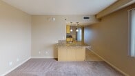 This single-floor unit at 801 Actionable City Blvd, #716 in National City offers a straightforward, functional layout with consistent warm neutral tones throughout. The open living area features plush wall-to-wall carpeting and receives generous natural light, particularly notable near the entry where sunlight casts bright patterns across the floor.

The kitchen is defined by a wraparound peninsula topped with speckled granite countertops, complemented by matching cabinetry in a warm yellow-toned finish. Pendant lighting hangs above the peninsula, adding a focused decorative element to the space. The kitchen flows openly into the living area, enhancing the sense of connectivity between spaces.

A separate carpeted room features a full-width sliding glass door fitted with vertical blinds, allowing filtered natural light and providing access to an outdoor view. This versatile space could serve as a bedroom or secondary living area.

The bathroom is finished with tile flooring, a granite-topped vanity with matching cabinetry, a large mirror, and a glass-enclosed walk-in shower with tiled surround. The unit is currently unfurnished, offering a clean slate for personalization.