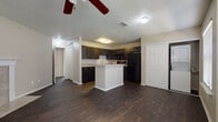 This single-floor unit offers a functional and cohesive layout designed for comfortable everyday living. The kitchen serves as a central focal point, showcasing rich dark cabinetry, granite-style countertops, and a full suite of black appliances including a refrigerator, range, and over-the-range microwave. A white peninsula provides additional prep space and creates a natural divide between the kitchen and the open living area, which is finished with rich, dark hardwood-style flooring throughout. Ceiling fans are present in multiple rooms, enhancing air circulation and comfort. The bedrooms are carpeted in warm neutral tones and each features a dedicated closet — one with a walk-in configuration complete with built-in shelving, and another with a reach-in closet. Large windows in the bedrooms allow for ample natural light to fill the space. The bathroom is well-equipped with a wide vanity topped with a granite-style surface, a large framed mirror, and a full soaking tub with tiled surround. Textured ceilings are consistent throughout the unit, adding a classic residential finish. Hallways connecting the rooms are bright and open, contributing to the overall sense of flow and accessibility within the space.