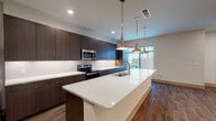 Located in Plano, Texas, this contemporary two-story residence at Windrose offers a thoughtfully designed interior with high-end finishes throughout. The open-concept kitchen serves as a centerpiece of the home, showcasing floor-to-ceiling dark espresso cabinetry, a crisp white subway tile backsplash, and stainless steel appliances including a built-in microwave and electric range. A generous quartz-topped island anchors the space, illuminated by a trio of polished pendant lights and positioned to overlook the living area. Wood-look tile flooring runs throughout the main living spaces, lending warmth and a cohesive aesthetic. The living and entry areas are open and airy, with large windows that invite natural light and offer views of the surrounding streetscape. Bedroom spaces feature soft carpeting, ceiling fans, and well-sized windows that continue the home's emphasis on natural light. The bathroom is elegantly appointed with marble-surround glass-enclosed shower, a dark wood floating vanity, white quartz countertops, and a backlit mirror. Spanning two floors, the layout provides a functional separation between living and private spaces, making this Plano residence a refined and modern place to call home.